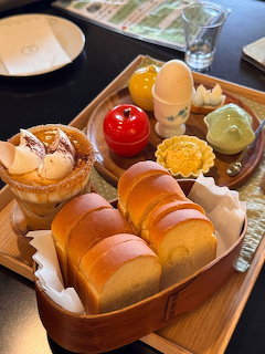 Wooden tray with assorted Japanese breakfast pastries, bread, colorful desserts, and drinks