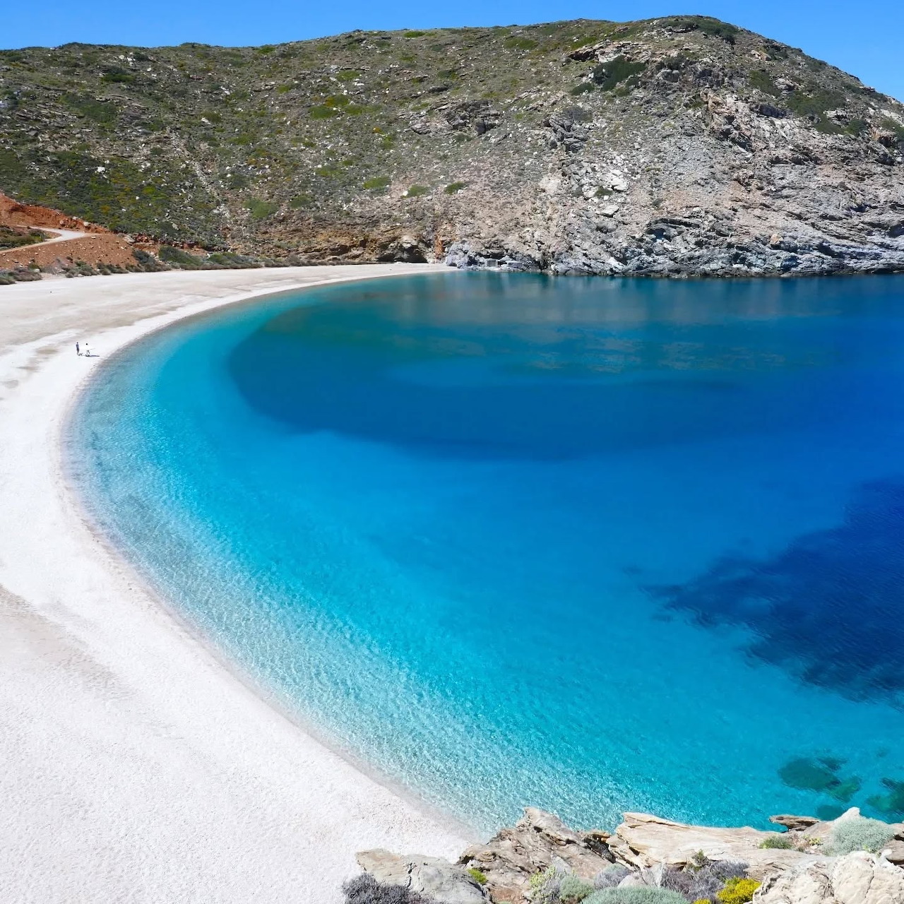White sand beach with turquoise water in a rocky cove under a clear blue sky