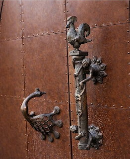 Ornate bronze door handle with roster, peacock, and mythical creature designs on a riveted metal door