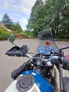 Blue motorcycle handlebars and windshield viewed from the rider's seat on a road lined with trees