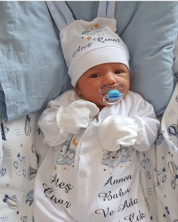 Baby wearing a white outfit and hat, lying on a blue cushion with a blue pacifier