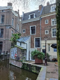 Historic brick buildings along a canal with a white structure displaying LOVE ME graffiti and a palm tree