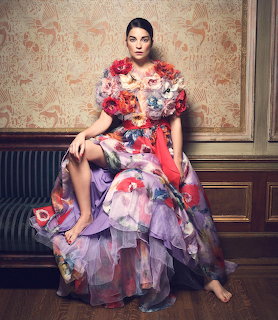 Woman in colorful floral gown with purple tulle skirt sitting on upholstered furniture in ornate room