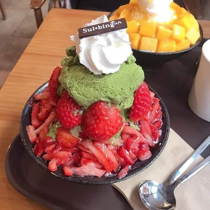Matcha strawberry bingsu topped with whipped cream and sliced strawberries on a tray