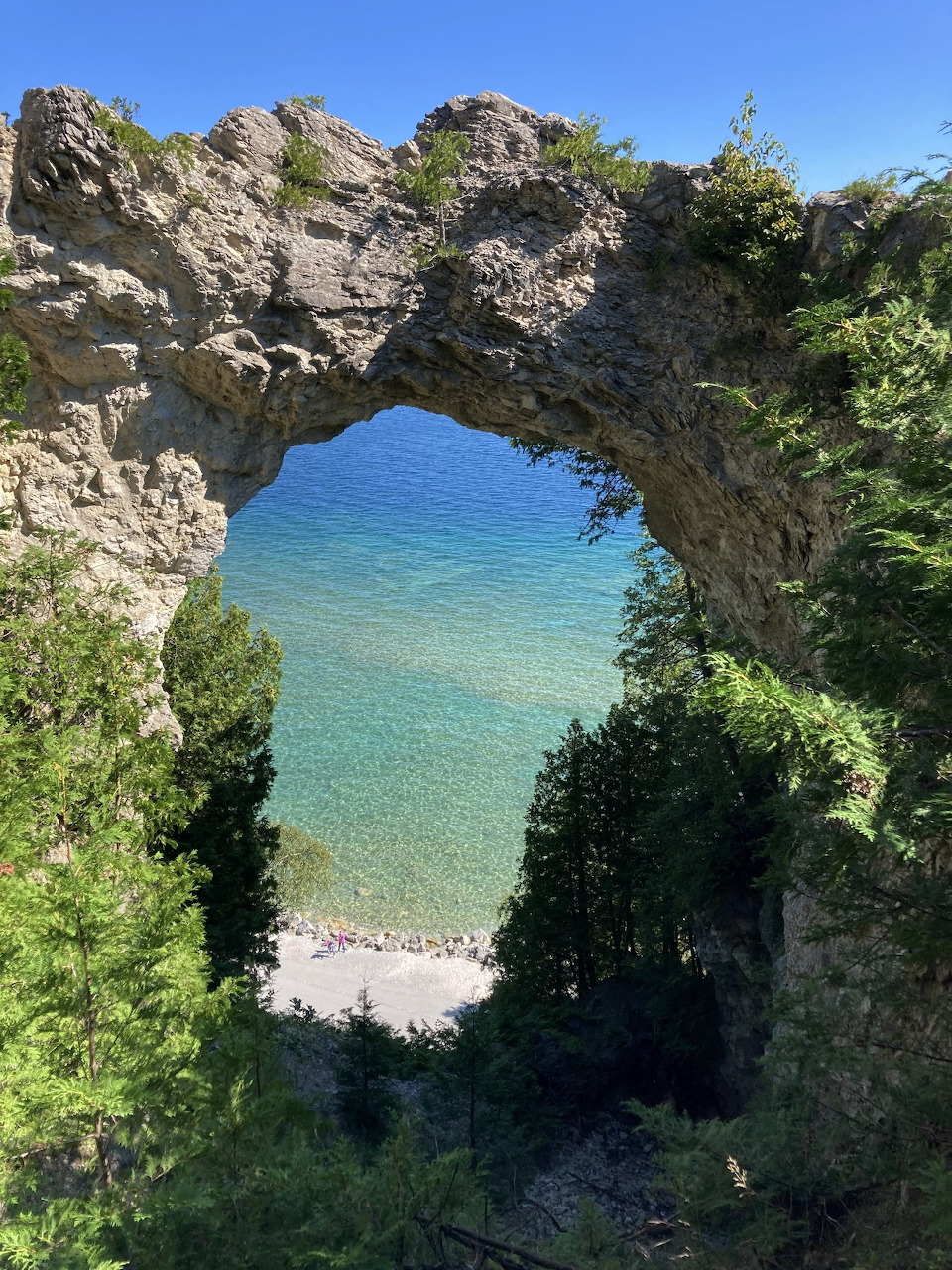 Natural rock arch framing turquoise lake water and a small beach below