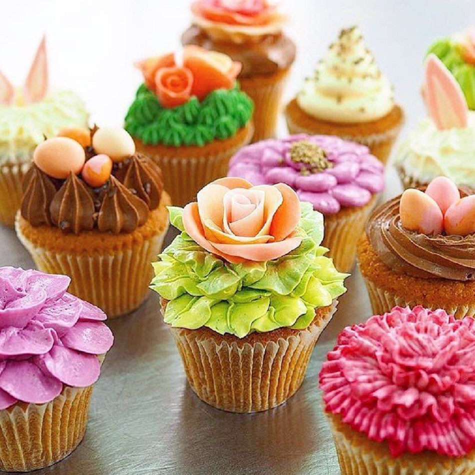 Assorted cupcakes decorated with colorful buttercream flowers including roses, daisies, and carnations