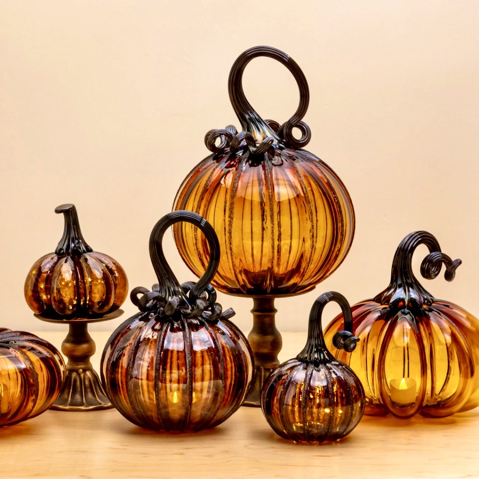 Several handblown glass pumpkins in orange and amber with ornate dark stems arranged in a group