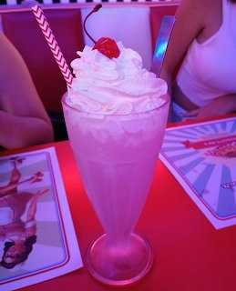 Tall milkshake glass topped with whipped cream and a cherry on a diner table with red lighting