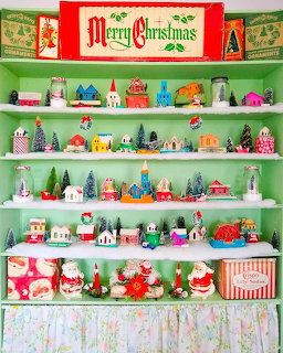 White shelves filled with vintage Christmas village houses, trees, and holiday decorations