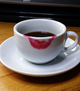 White coffee cup with a lipstick mark on the rim, resting on a saucer on a wooden table.