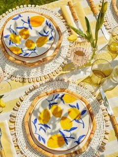 Two place settings with lemon-decorated plates on yellow gingham tablecloth with white tulips