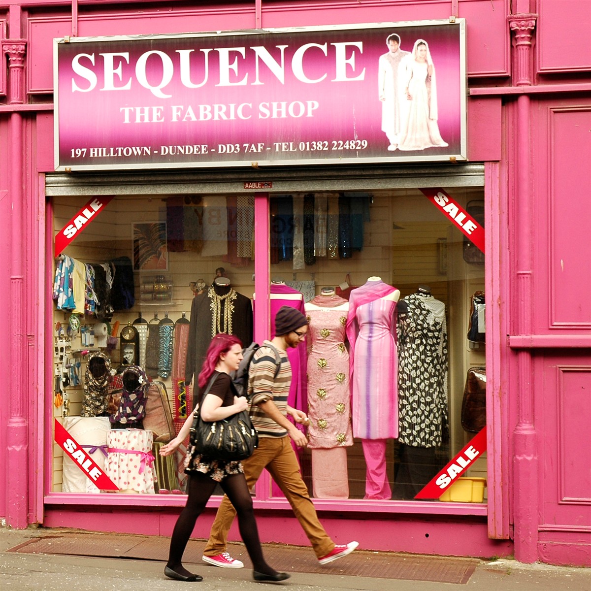 Bright pink storefront of Sequence fabric shop with mannequins in window display and people walking by