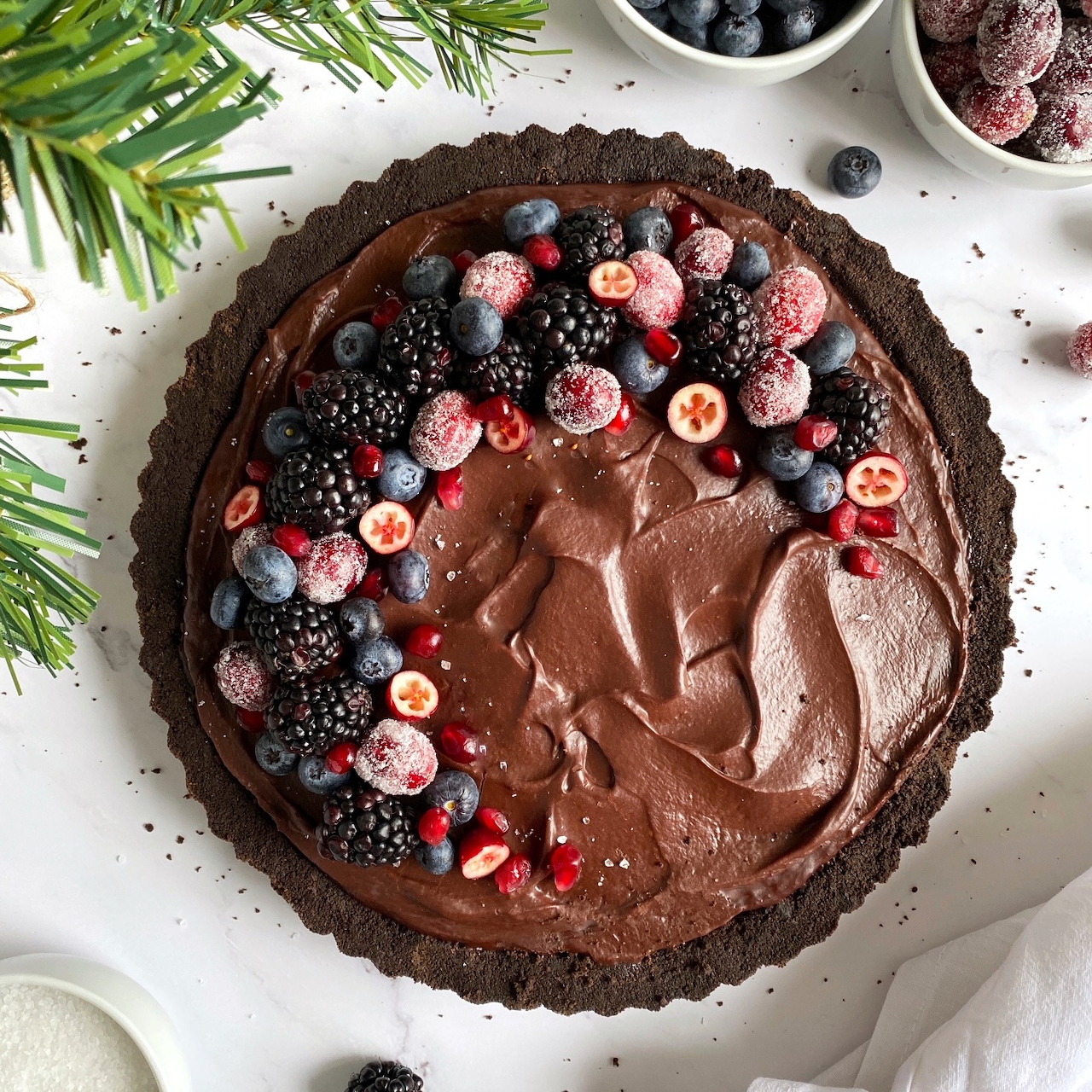 Overhead view of a dark chocolate tart topped with fresh berries and chocolate ganache in a fluted crust