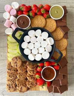 Dessert board with cookies, marshmallows, strawberries, chocolate sauce, and candies on wood surface