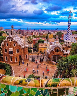 Colorful mosaic terrace and gatehouses at Park Güell in Barcelona with city skyline and dramatic sky