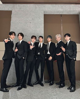 Seven young men in black suits posing together indoors