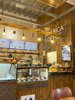 Wooden cafe interior with pendant lights, pastry display case and Arabica coffee sign