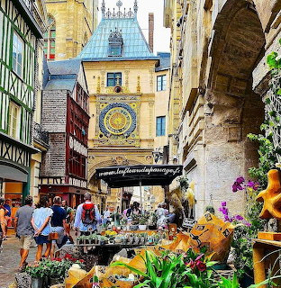 Medieval clock tower and half-timbered buildings on cobblestone street in Rouen with flower market stalls