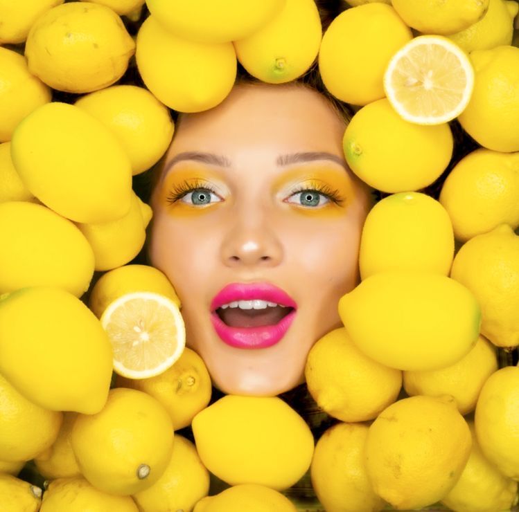 Close-up of a woman’s face surrounded by bright yellow lemons