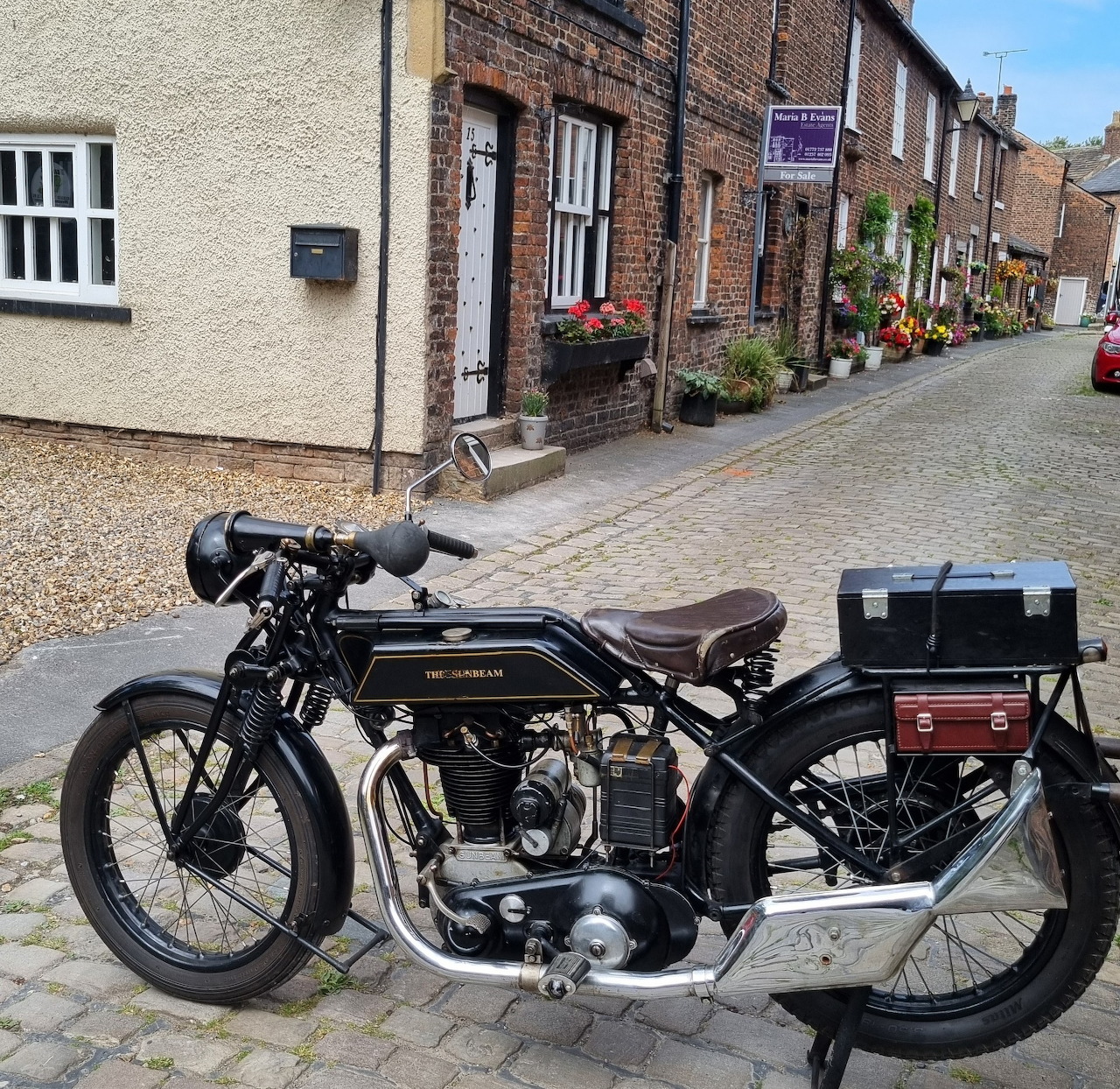 Vintage black Sunbeam motorcycle on cobblestone street in traditional British village