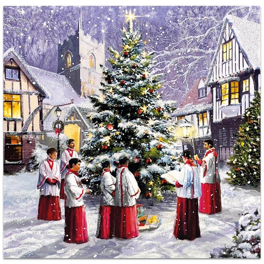 Children's choir singing around Christmas tree in snowy village with church and illuminated Tudor houses