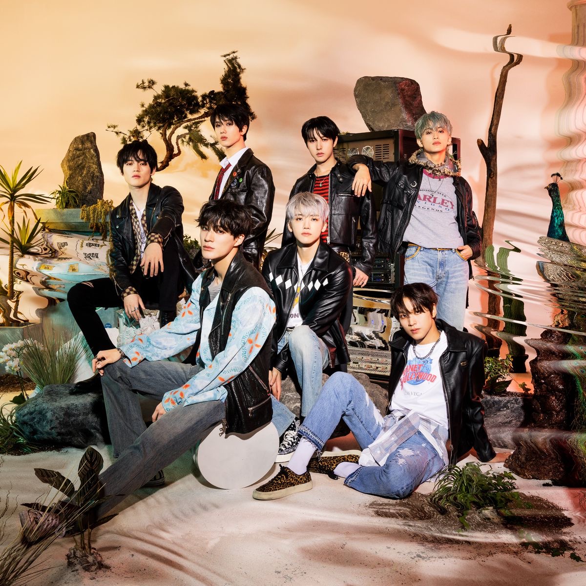 Seven NCT Dream members posing together on a colorful tropical-themed set with painted sky backdrop