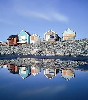 Row of colorful beach huts on rocky shore reflected in still blue water
