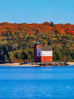 Red lighthouse on shore with autumn trees and blue water