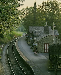 Empty curved railway platform with old stone station house nestled among green trees