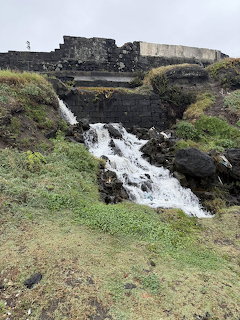 Small brook flowing over rocks with green grass and old stone ruins in the background