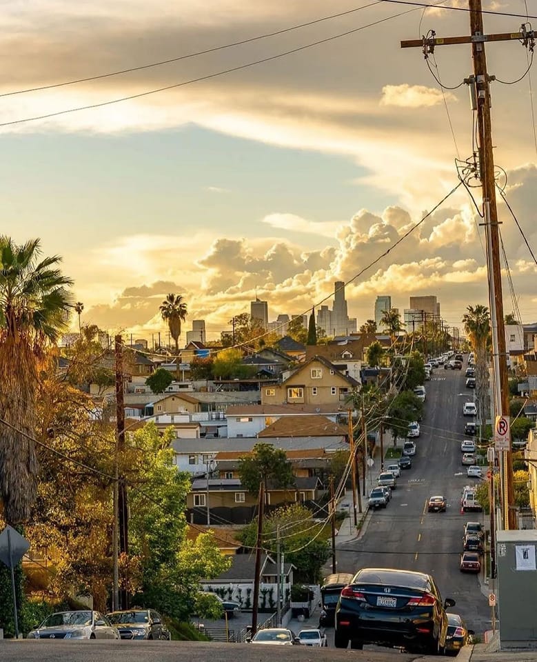 Sunset view down residential street in East Los Angeles with palm trees and downtown skyline in distance