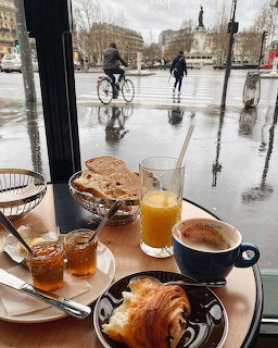 French breakfast with croissants, coffee, and orange juice on a table by a rainy Parisian café window