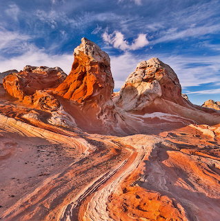 Striped sandstone rock formations in warm orange and white tones against blue sky