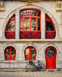 Art Nouveau building with red ornamental doors and arched windows, bicycle leaning against cream stone facade