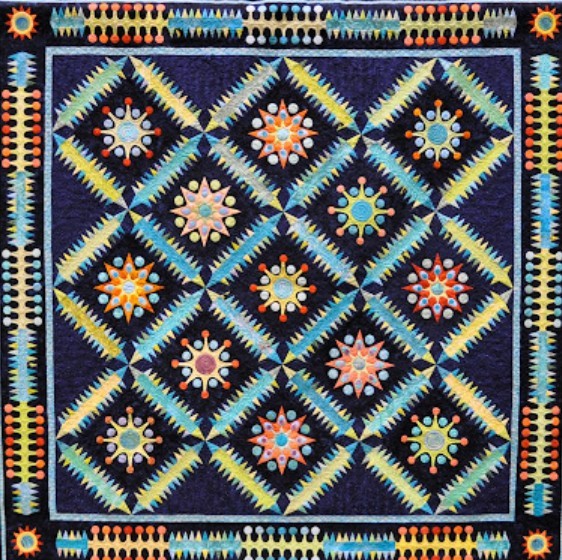 Geometric quilt with repeating star patterns in orange, blue, and yellow on navy background