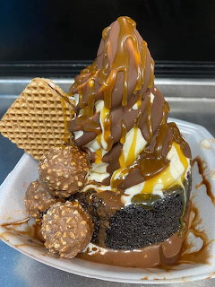 Ice cream sundae with caramel sauce, whipped cream, wafer cone and brownie on white plate