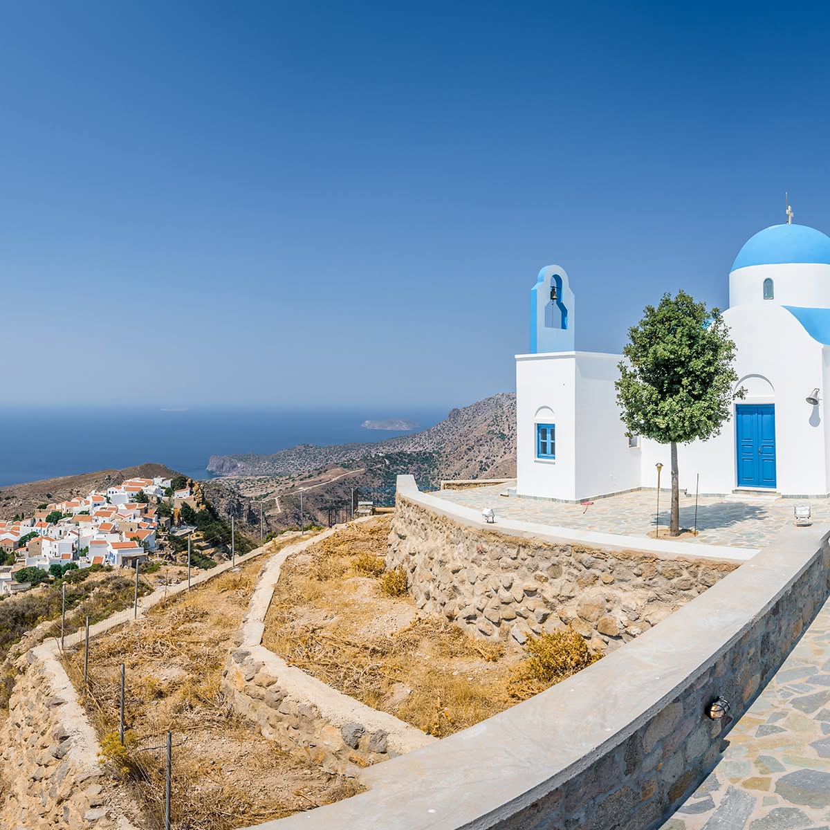 White church with blue dome on a hillside above a coastal village and the sea