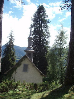 Small stone chapel with wooden steeple surrounded by tall pine trees and mountains in Samoëns, France