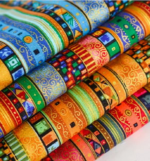 Multiple rolls of colorful patterned fabric with geometric and decorative designs arranged diagonally