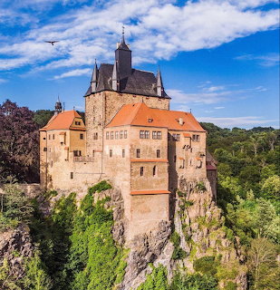 Kriebstein Castle on a rocky cliff surrounded by green trees under a blue sky