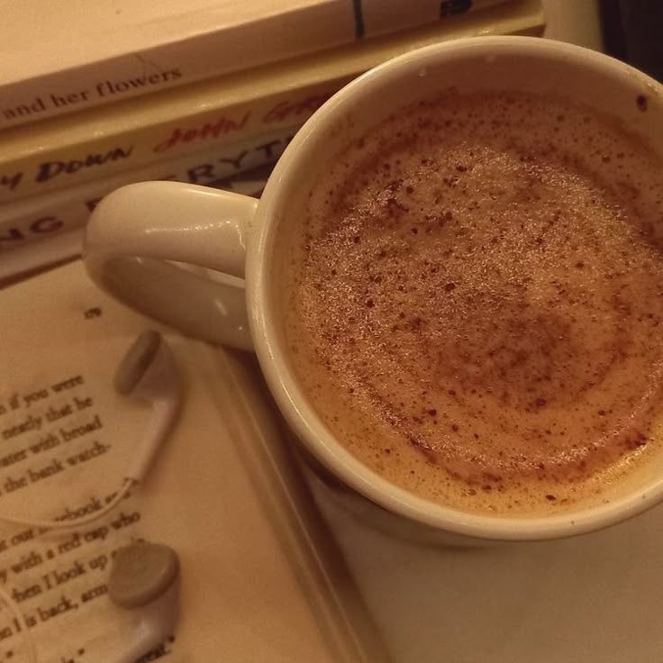 White coffee mug with foam beside open book pages on table