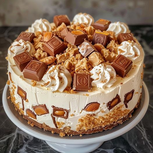 Decorated layer cake with caramel, chocolate, whipped cream, and candy pieces on white stand