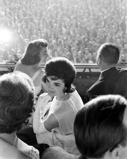 Black and white photo of Jackie Kennedy smiling among a crowd at the 1961 presidential inauguration