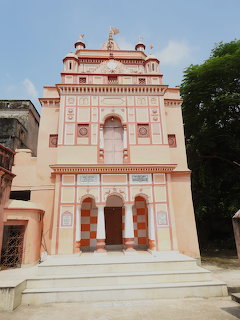 Pink and white Hindu temple with ornate facade, arched doorway, and white steps leading to entrance