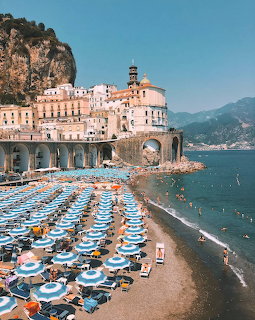 Atrani beach with rows of blue striped umbrellas, white buildings on cliffside, mountains and sea in background