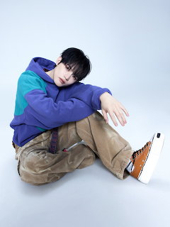 Young man with black hair sitting on floor wearing blue jacket and beige cargo pants
