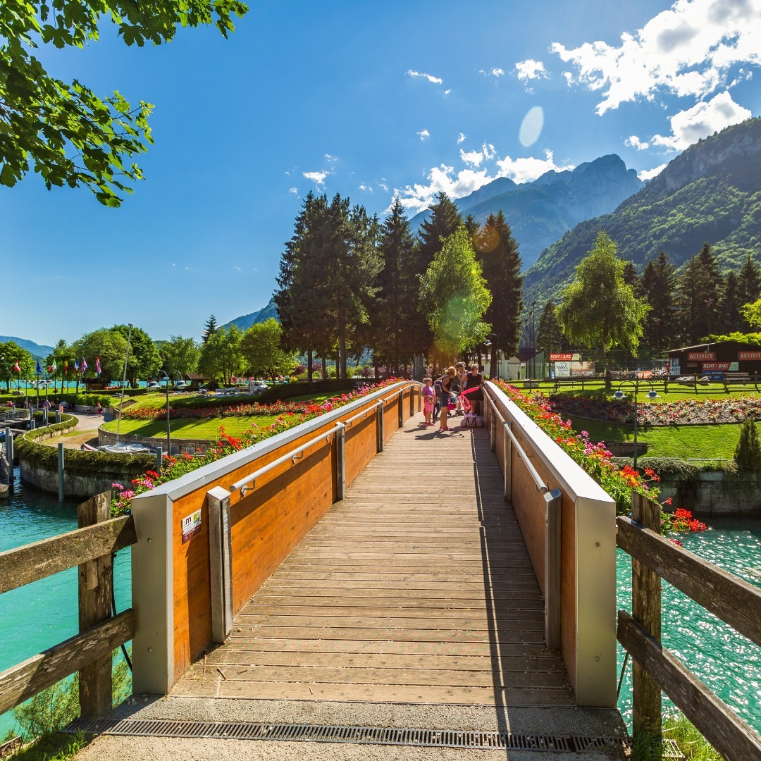 Wooden pedestrian bridge crossing turquoise lake with mountains and trees in background