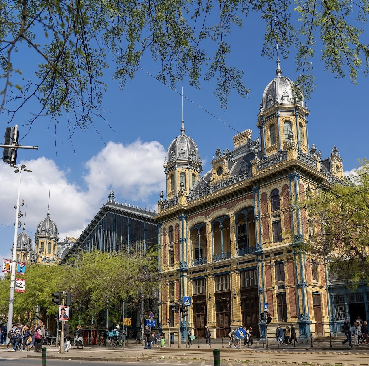 Nyugati Railway Station in Budapest with ornate facade, twin towers, and glass train shed behind trees