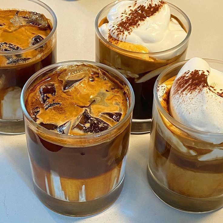 Four layered coffee drinks in clear glasses with ice cubes and whipped cream topping