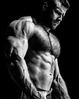 Black and white photo of a muscular bearded man with defined abs and chest in dramatic lighting